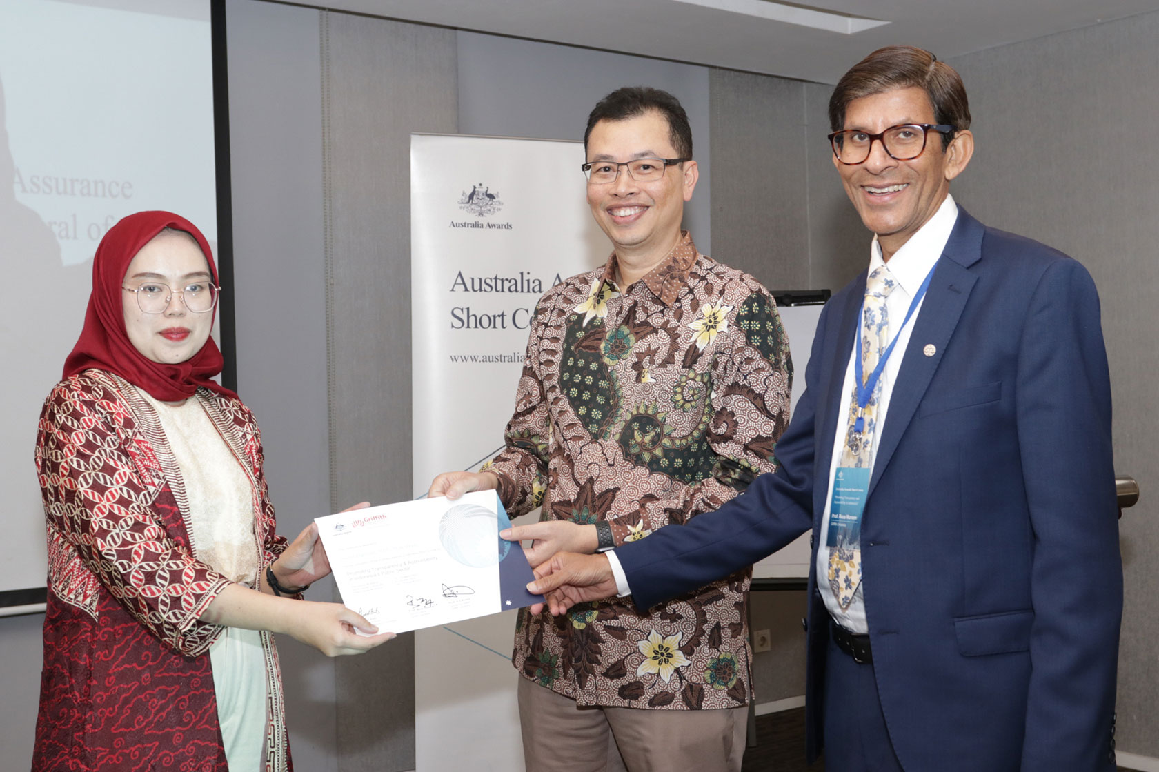 Professor Erwan Agus Purwanto and Professor Reza Monem hand the certificate of course completion to Siska Haryani, a participant from the Directorate General of Immigration. 