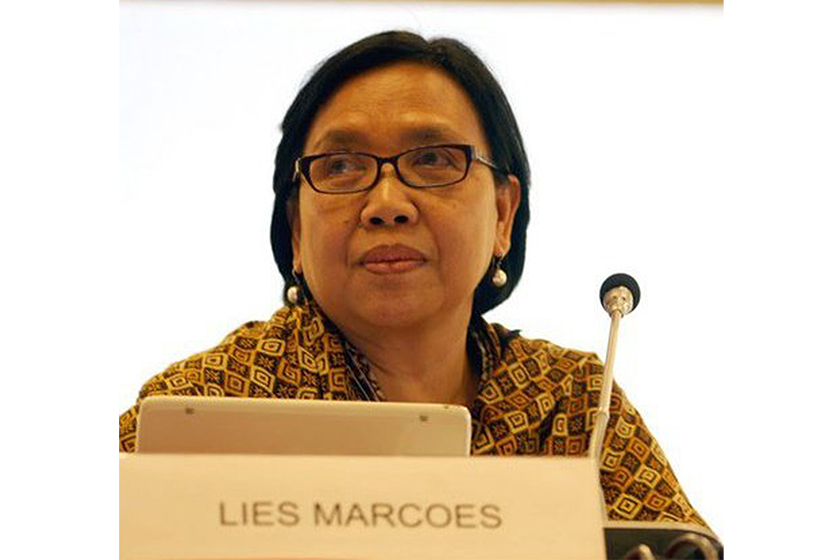 An older woman with glasses sitting with a microphone in front of her