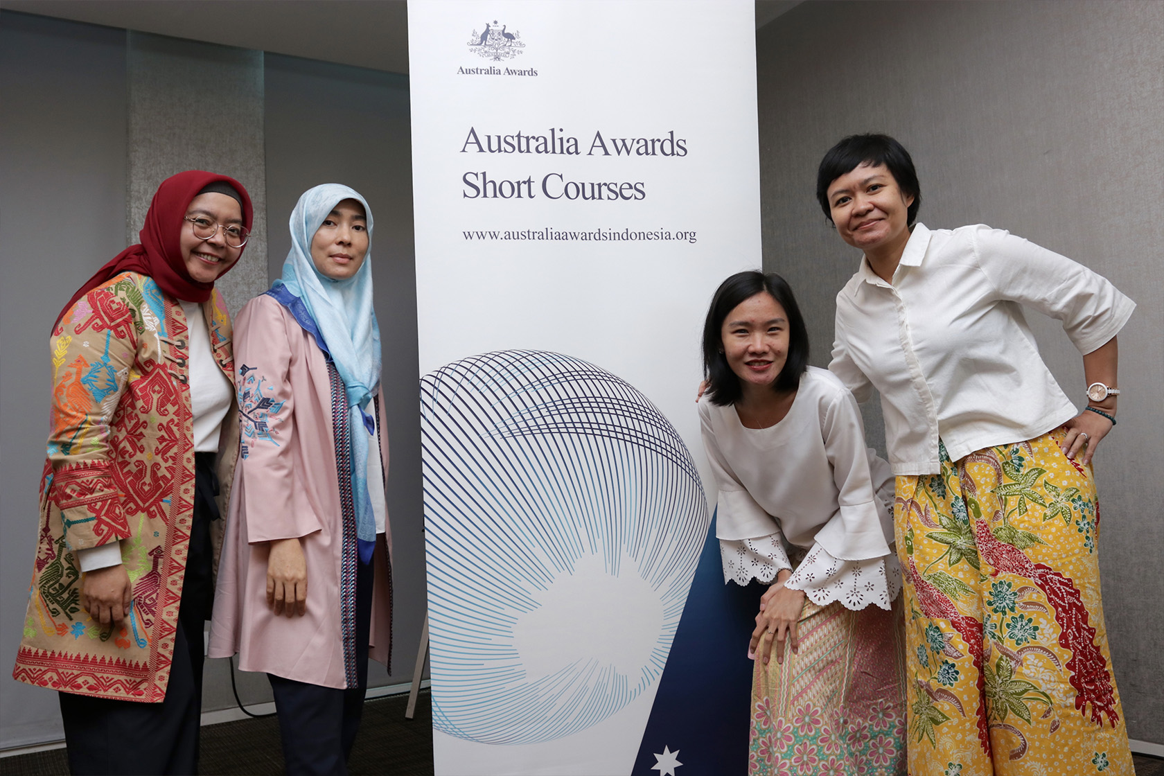 Four alumnae are standing and posing with Australia Awards Short Course standing banner