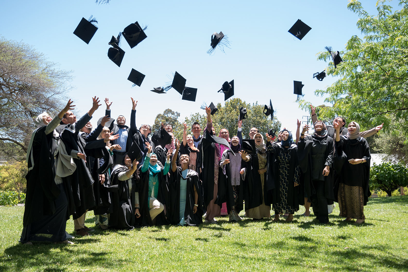 SSMP graduates smiling and throwing up their mortarboards in an outdoor scene