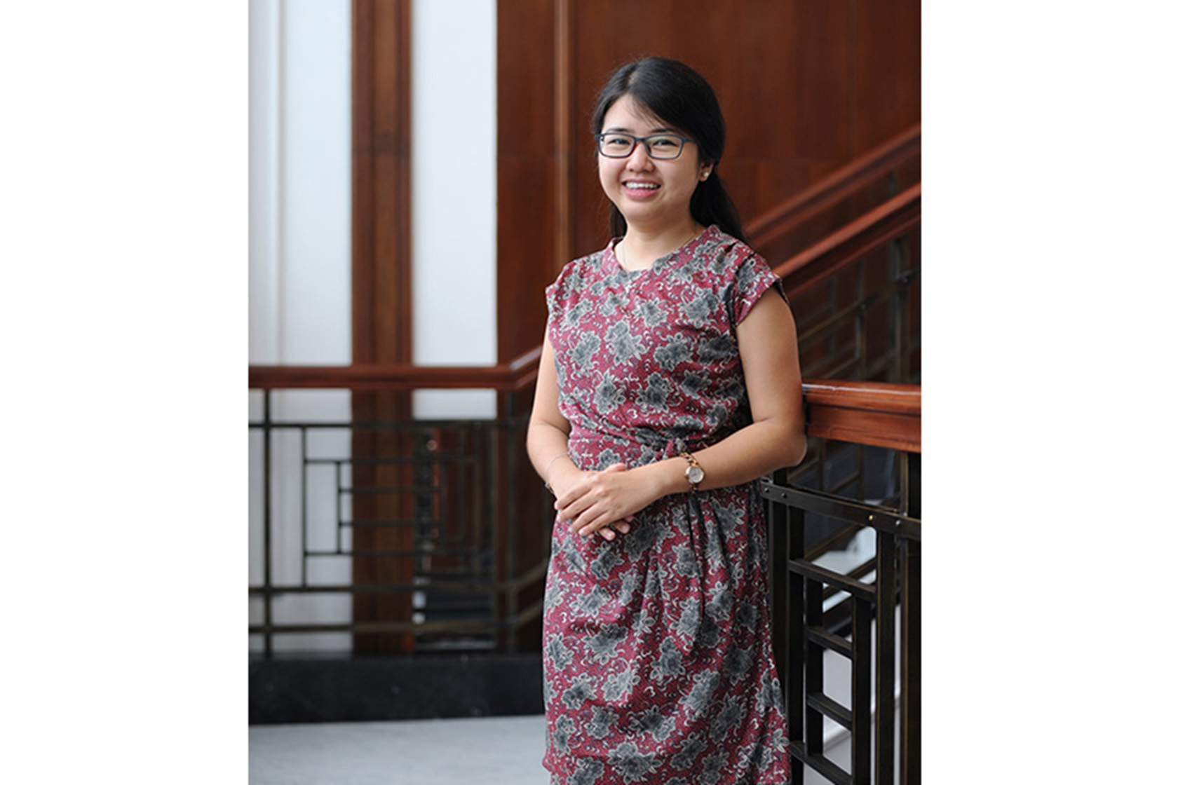 A woman with glasses and batik dress is standing in front of staircase