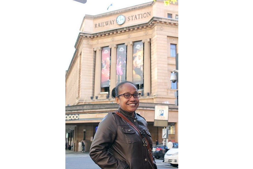 A woman with glasses and black jacket is standing in front of railway station