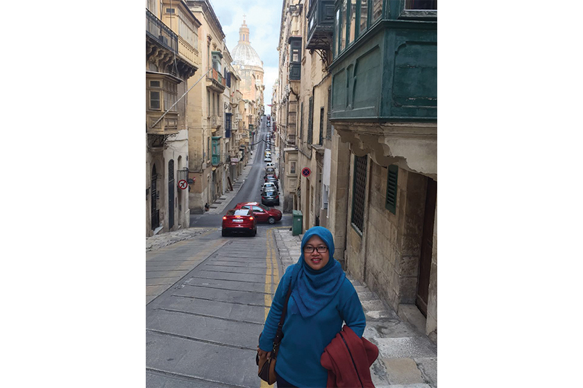 A woman with blue hijab wearing blue long sleeve tshirt standing on the pedestrian