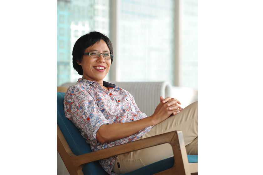 A smiling woman wearing patterned shirt sitting on the sofa