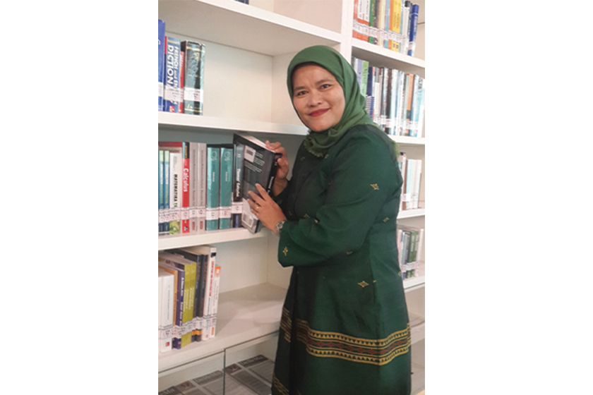 A woman with green hijab w earing green dress is taking a book from the book shelf